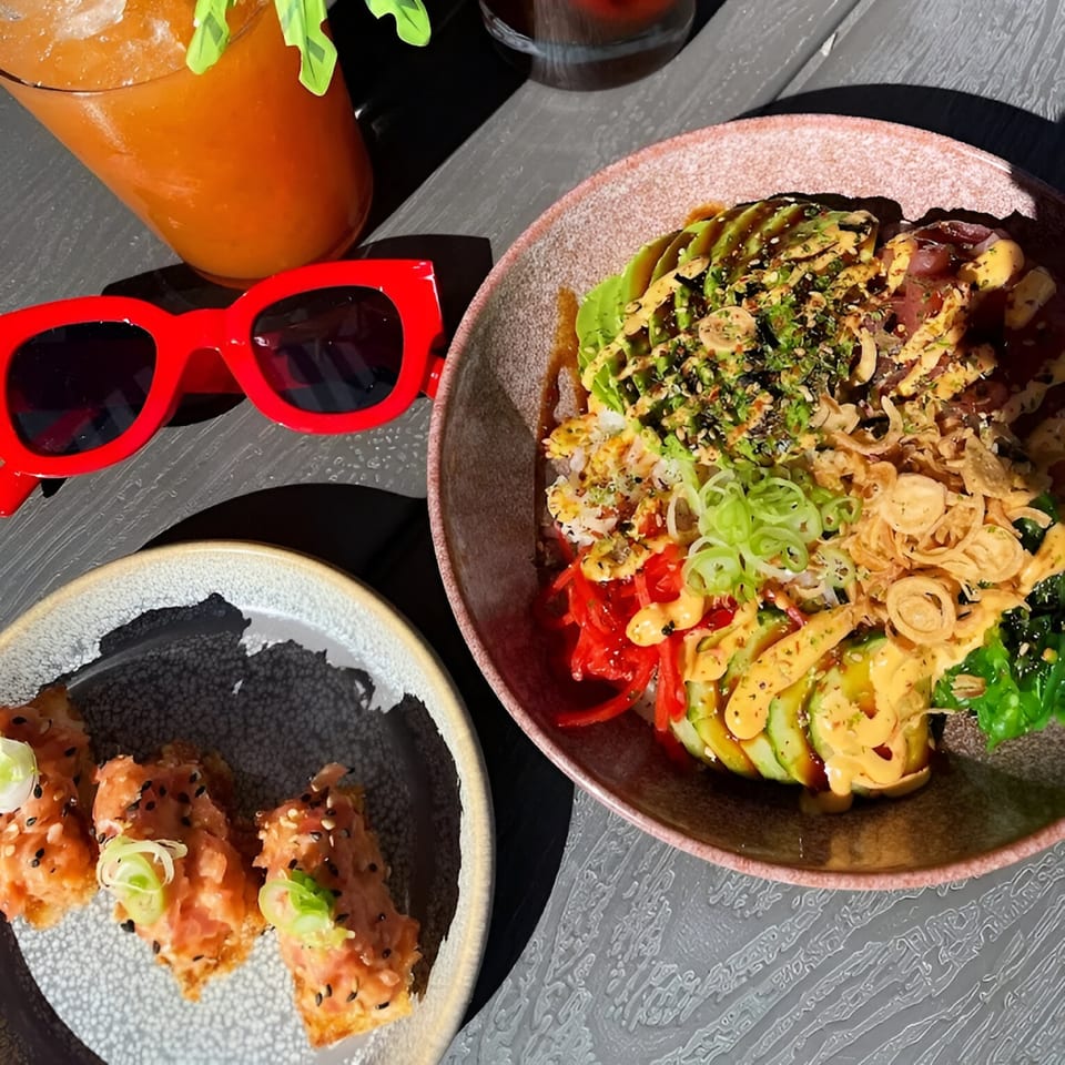 A Poke-San poke bowl with avocado, tuna, and toppings, alongside tuna crispy rice and a drink.