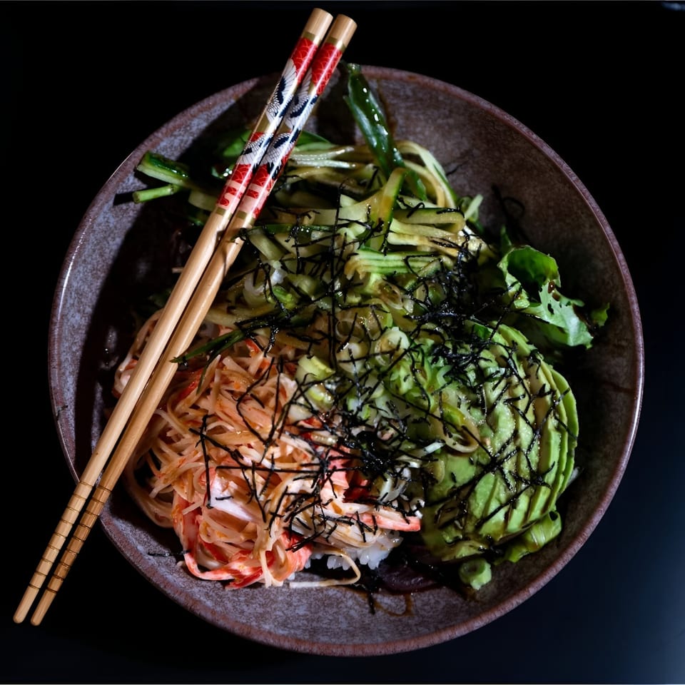 Poke-San poke bowl with crab, avocado, cucumber, and seaweed, with chopsticks resting on the rim.
